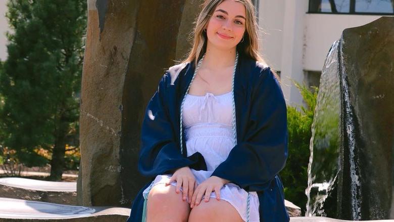 Sam Hagenbush wearing graduation cap sitting in front of fountain